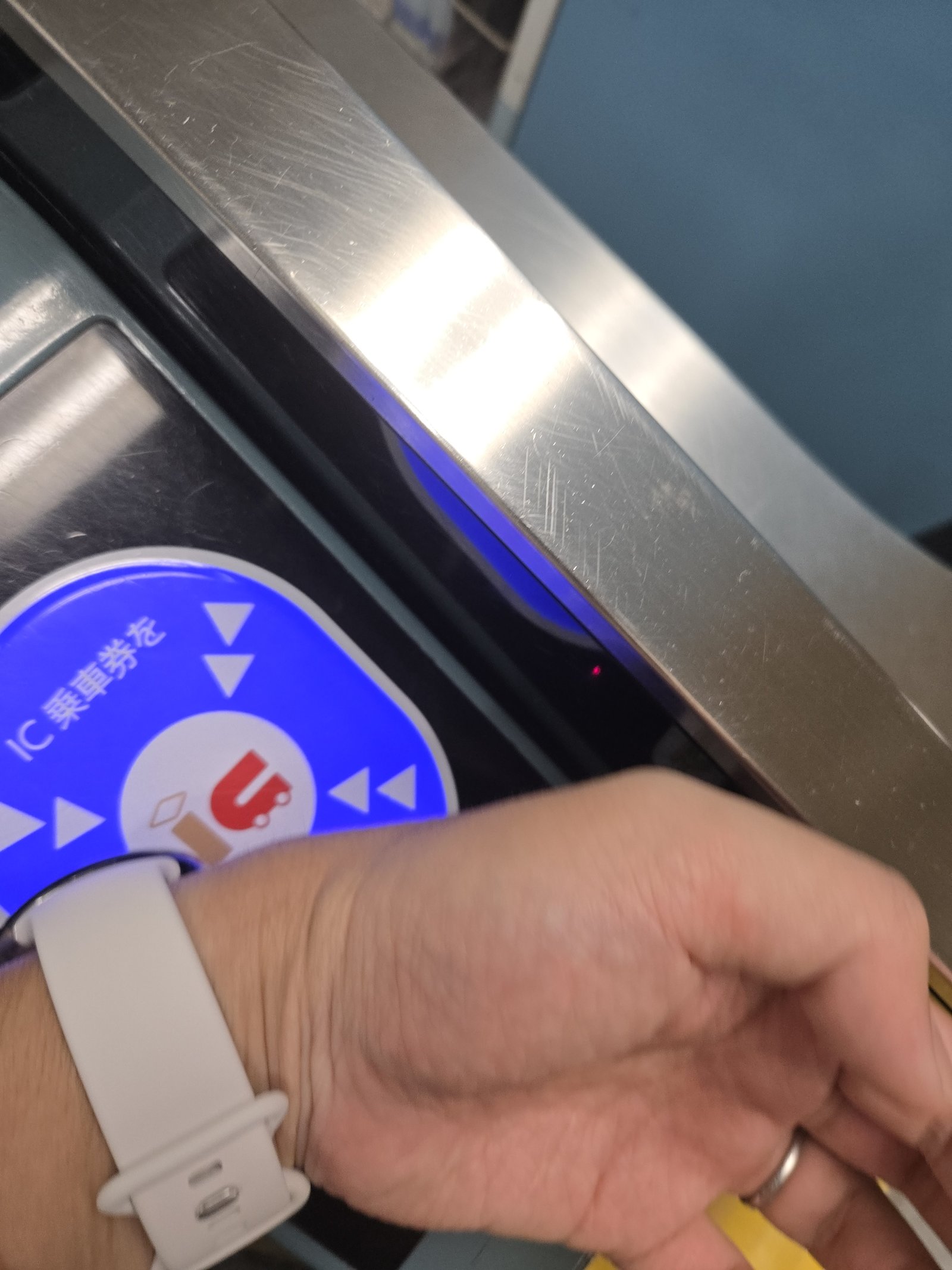A traveler tapping a smartwatch on an IC card reader at a Tokyo ticket gate.