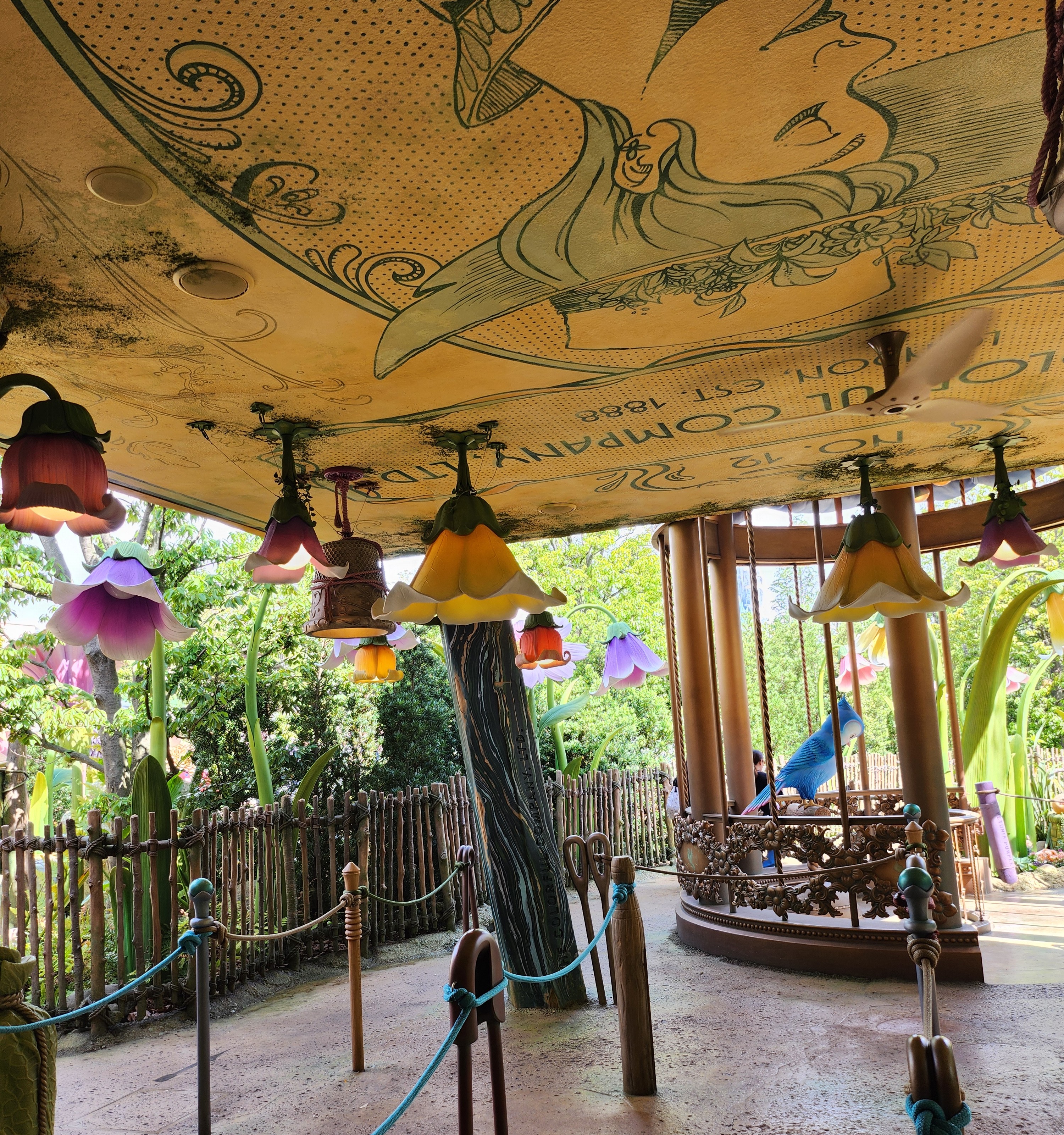 A decorated garden canopy area in the Fantasy Springs section of Tokyo DisneySea, with a small ride visible in the background.