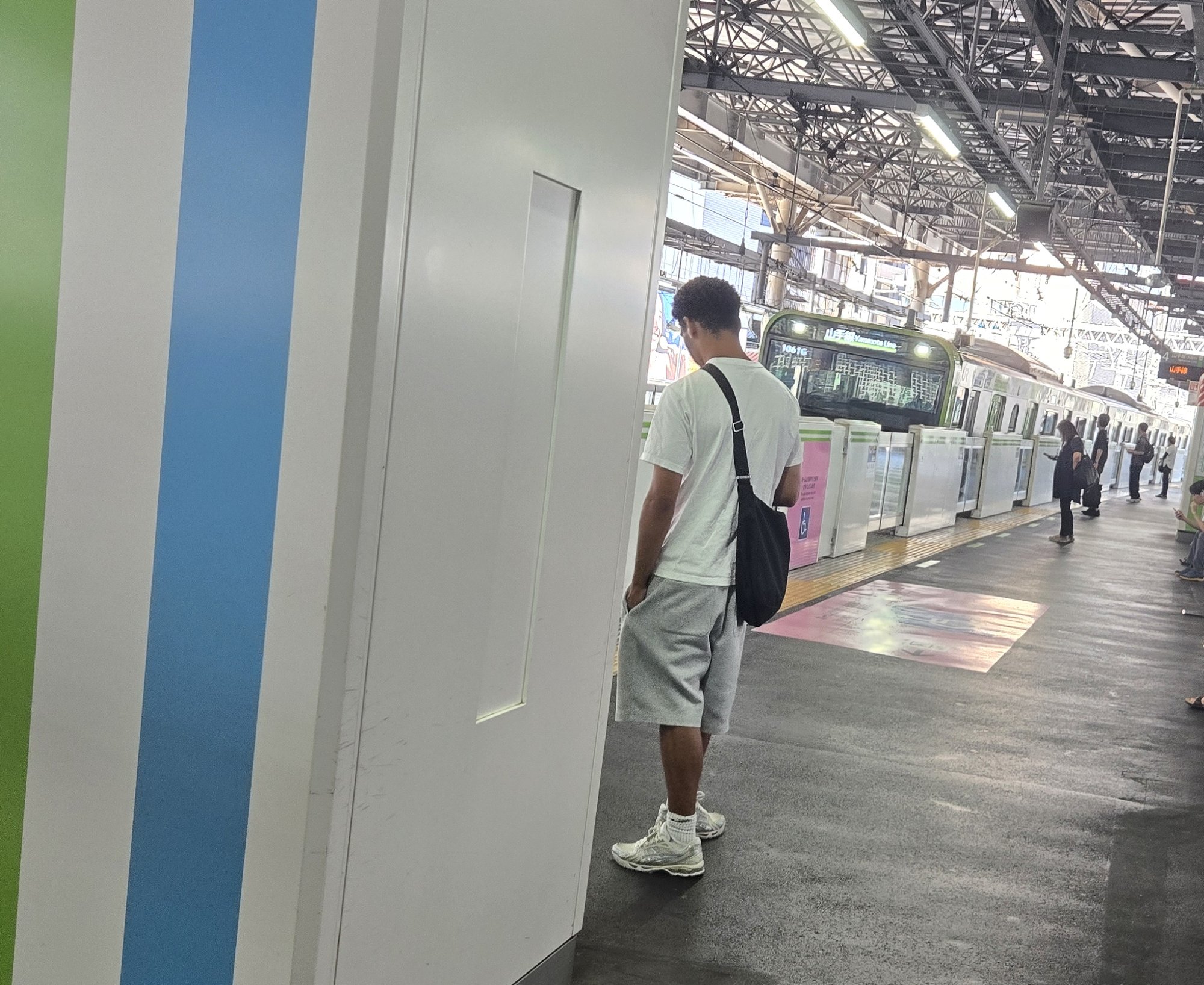 A passenger waiting on a JR train platform as a Yamanote Line train arrives in Tokyo.