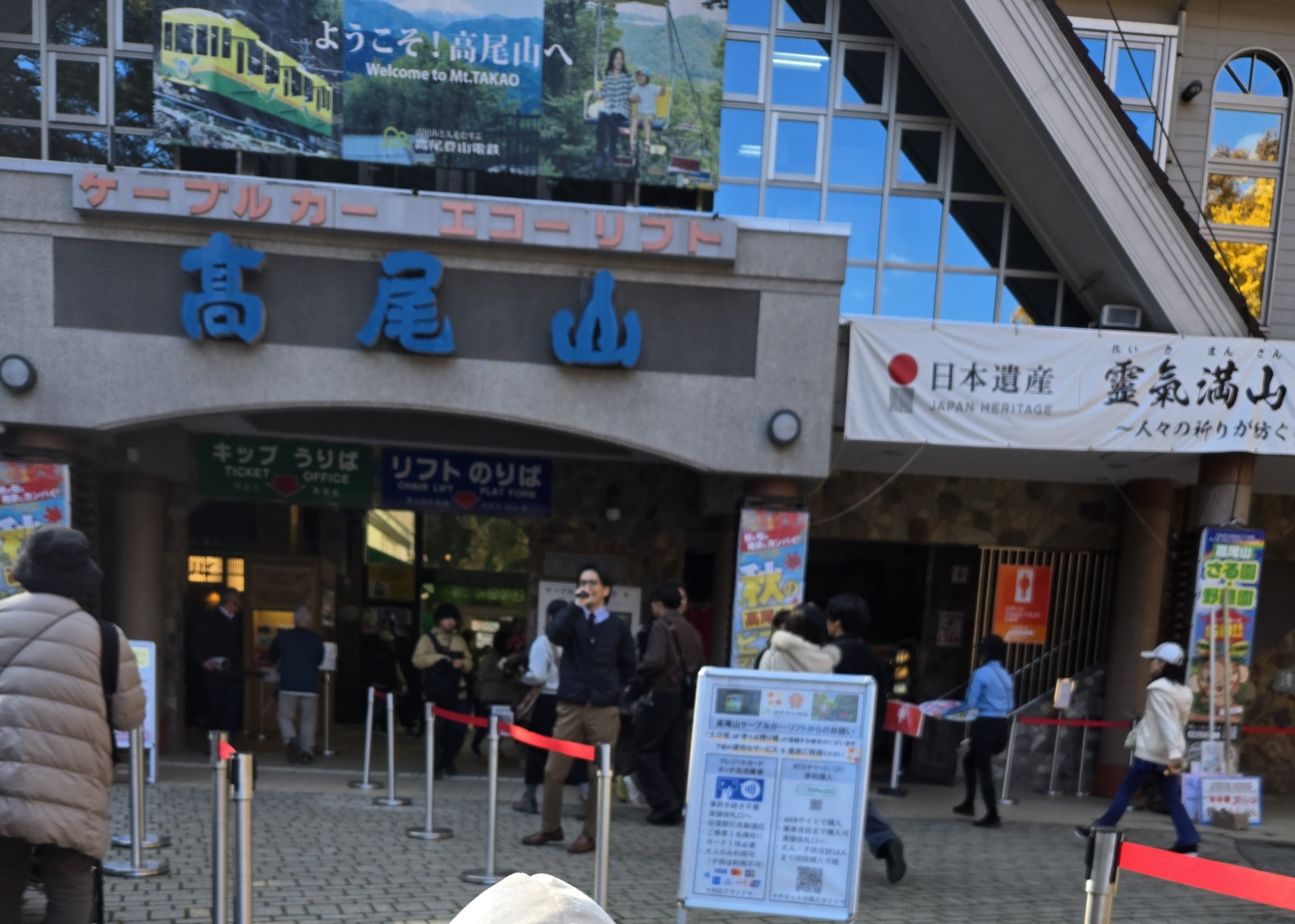 Ticket building for Takao Tozan Railway's cable car and Echo Lift chairlift at the base of Mount Takao, with a crowd of visitors during autumn foliage season.