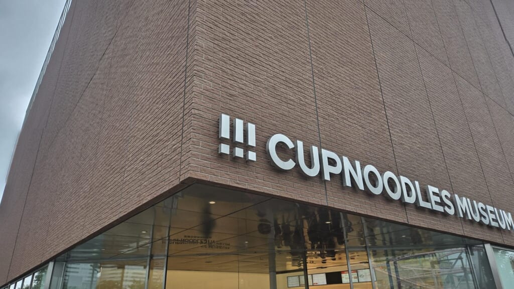 The Cup Noodles Museum Yokohama building, with the CUPNOODLES MUSEUM sign on its brick facade above the glass entrance.