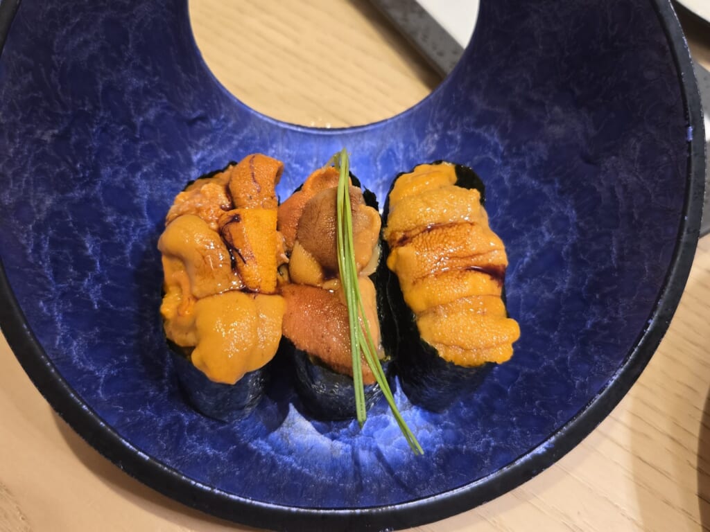 Three pieces of uni gunkan sushi in a deep blue bowl at Kaiten Sushi Ginza Onodera in Omotesando.