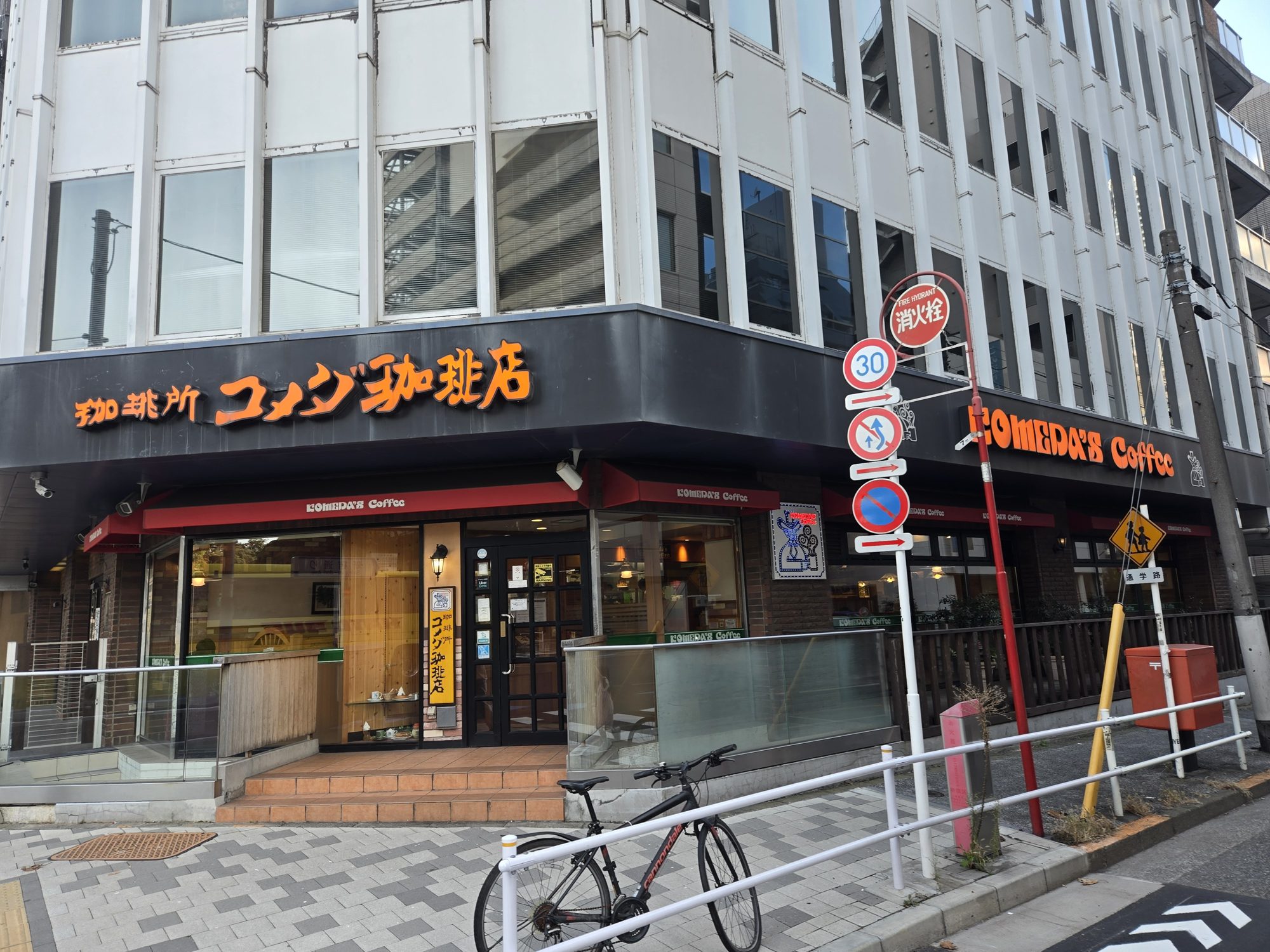 The corner storefront of Komeda's Coffee near Shinjuku-gyoemmae Station in Tokyo, with its orange sign above the entrance.