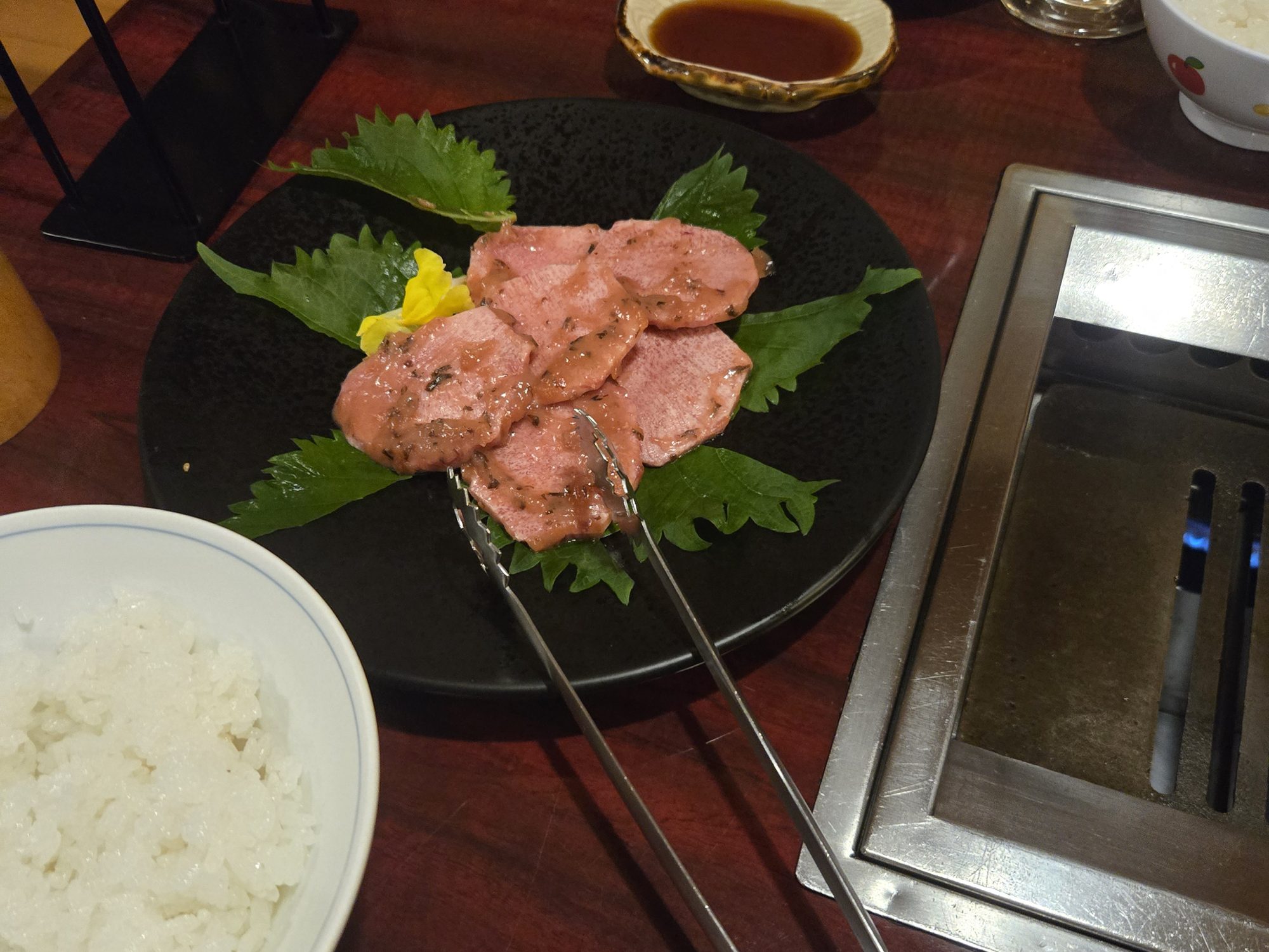 A plate of ume tan-shio, thin slices of salted beef tongue with plum, on shiso leaves next to the table grill at Rashomon in Yotsuya.