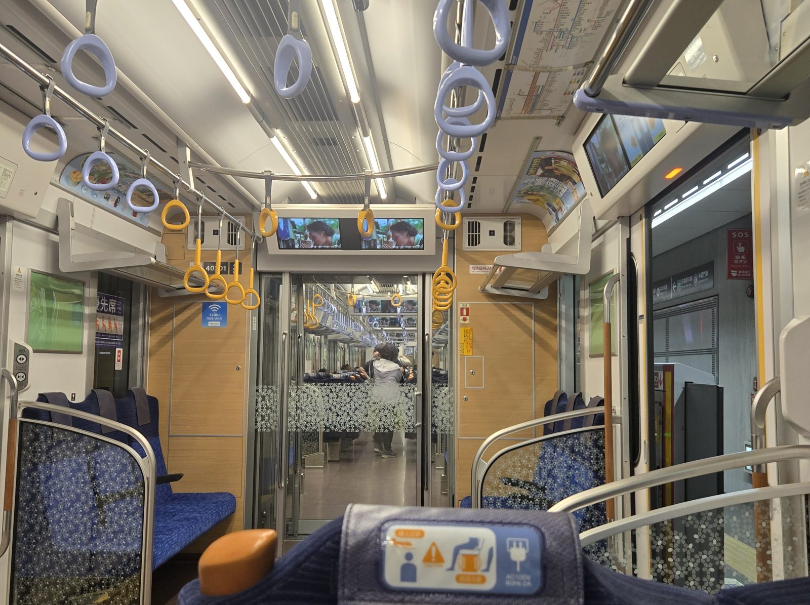 Interior of an S-Train car with blue seats, hanging straps and overhead information screens.