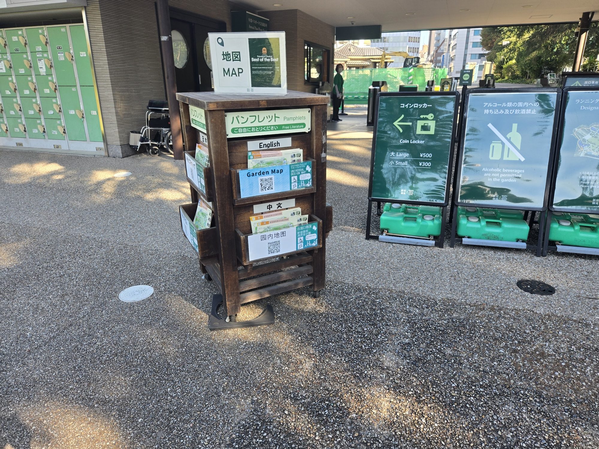 A wooden rack of free garden maps in English, Chinese, and Japanese next to coin lockers just inside Shinjuku Gyoen's Okido Gate.